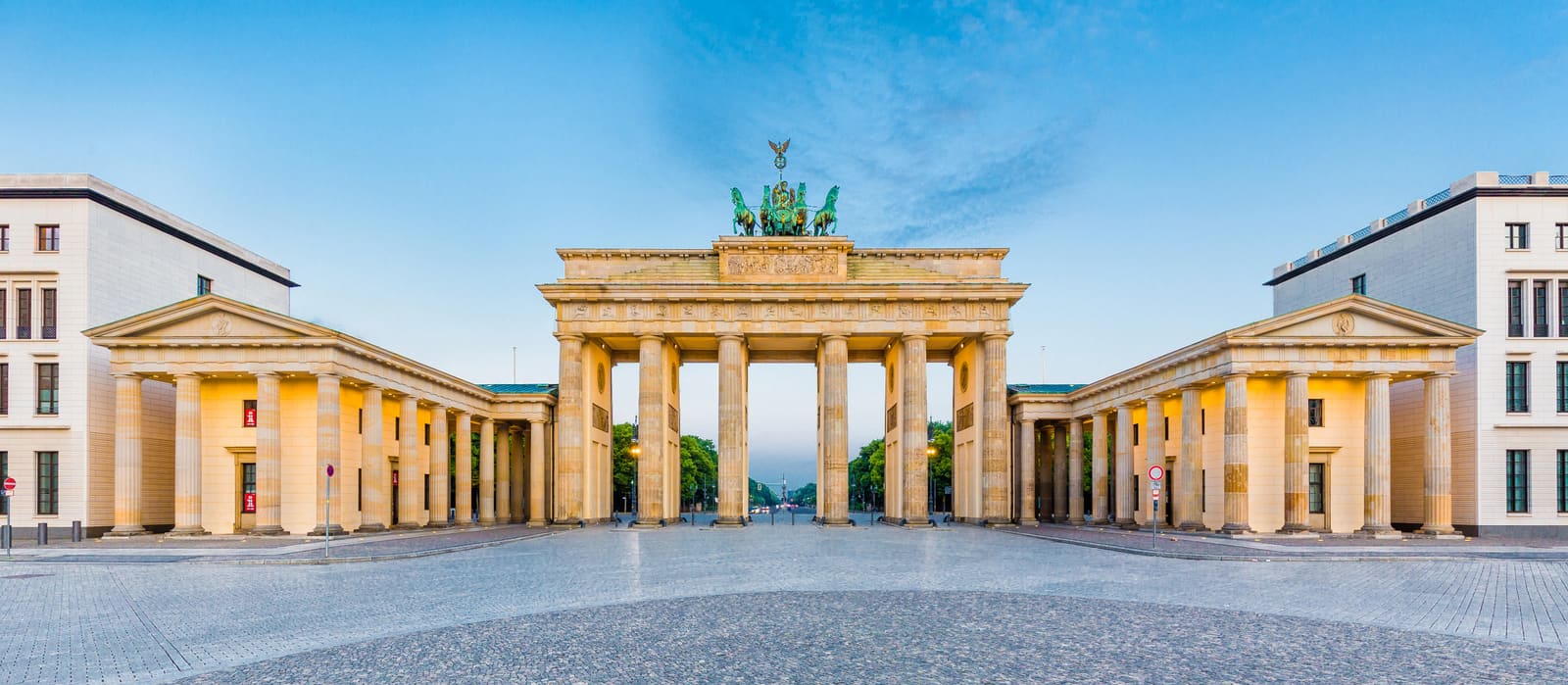 Das menschenleere Brandenburger Tor am frühen Morgen mit warm beleuchteten Säulen unter blauem Himmel