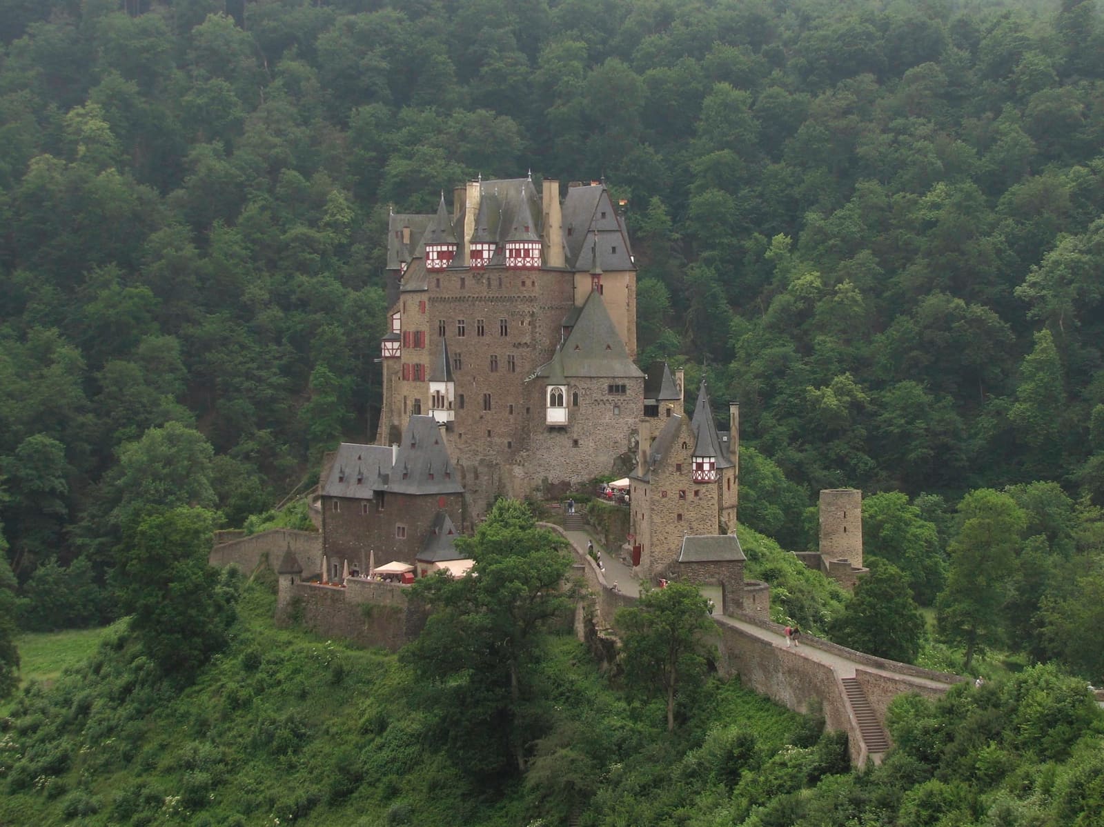 Burg Eltz mit hohen Schieferdächern, Fachwerkerkern und steinerner Zufahrt inmitten eines dicht bewaldeten Tals