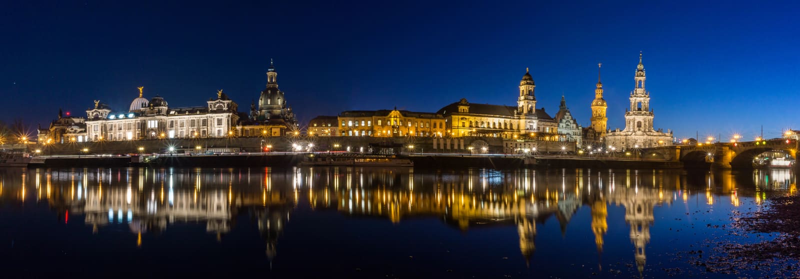 Beleuchtete Dresdner Altstadt an der Elbe in der blauen Stunde mit Hofkirche, Frauenkirche und spiegelnder Uferfront