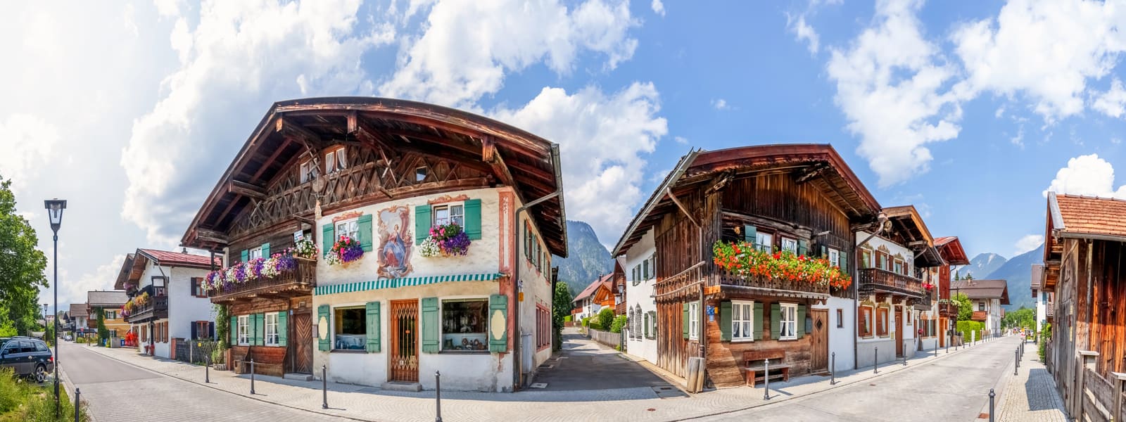 Historische Holzhäuser in Garmisch-Partenkirchen mit Lüftlmalerei, grünen Fensterläden, Blumenkästen und Bergen im Hintergrund