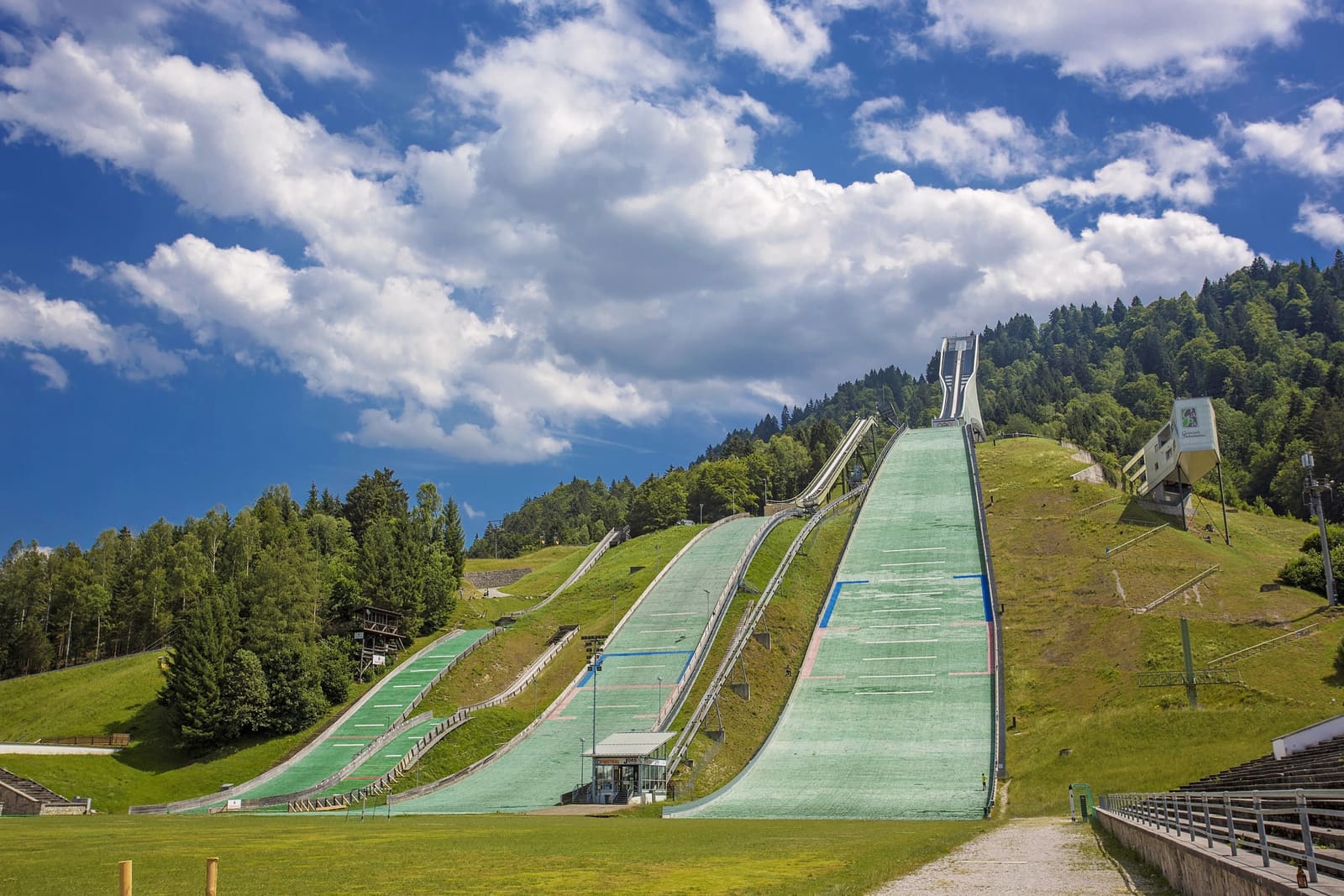 Olympische Skisprungschanzen in Garmisch-Partenkirchen mit grünen Matten vor bewaldeten Hängen