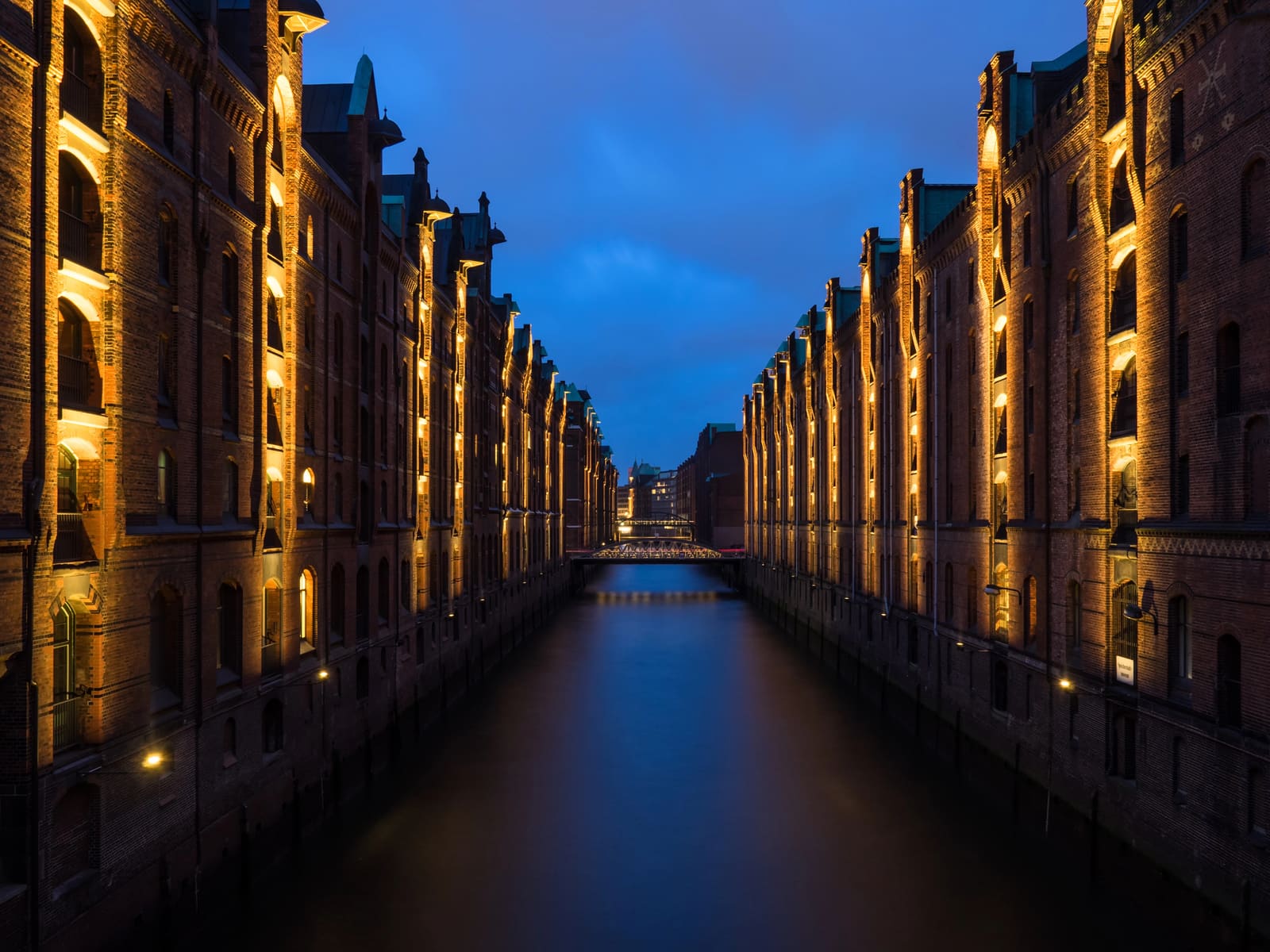 Beleuchtete Backsteinspeicher der Hamburger Speicherstadt zu beiden Seiten eines ruhigen Fleets in der blauen Stunde