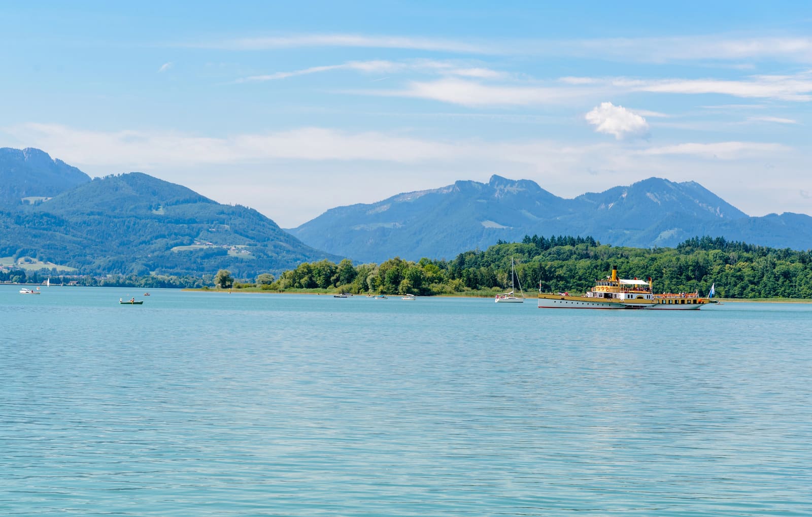 Historisches Fahrgastschiff auf dem Chiemsee vor bewaldetem Inselufer und den Bergen des Chiemgaus