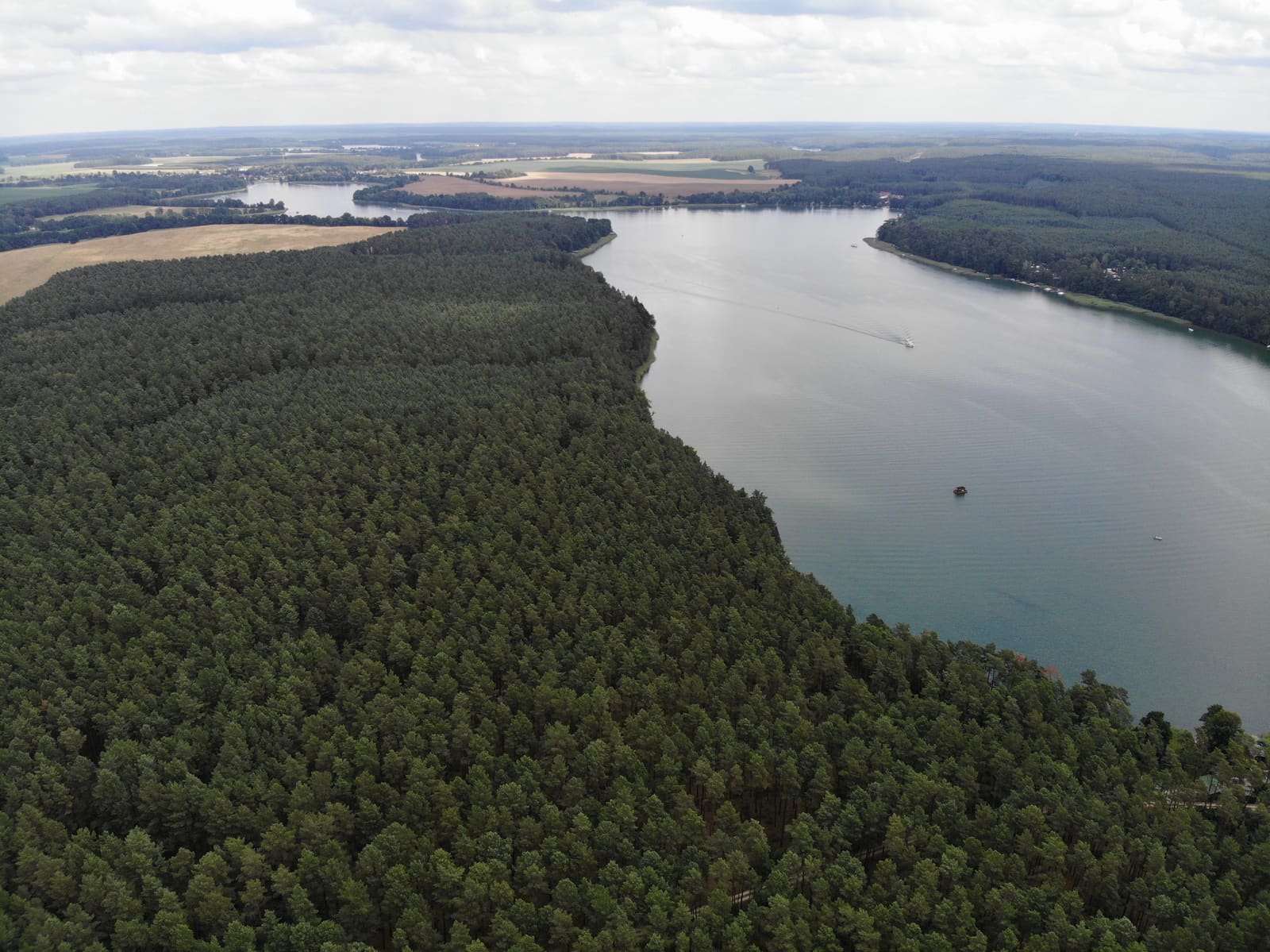 Luftbild des Großen Pälitzsees mit bewaldeten Ufern, kleinen Booten und weiteren Seen zwischen Feldern am Horizont