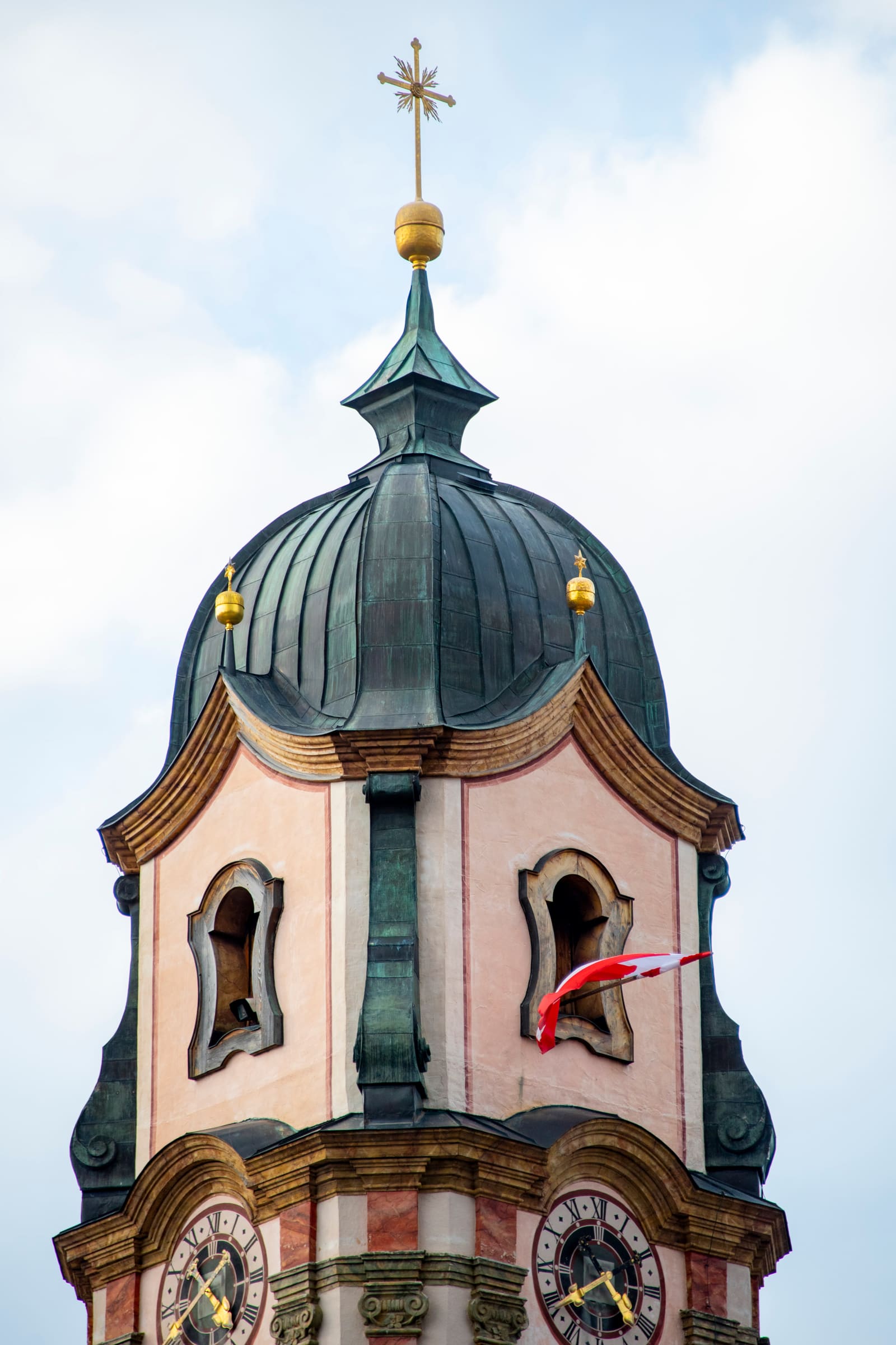 Barocker Kirchturm von St. Peter und Paul in Mittenwald mit rosafarbener Fassade, Uhren und kupferner Zwiebelhaube