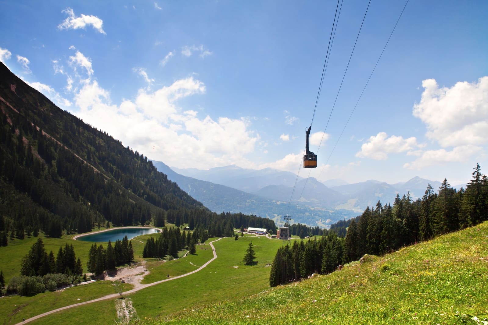 Kabine der Nebelhornbahn über grünen Almwiesen mit Bergwald, Speichersee und Allgäuer Alpenpanorama