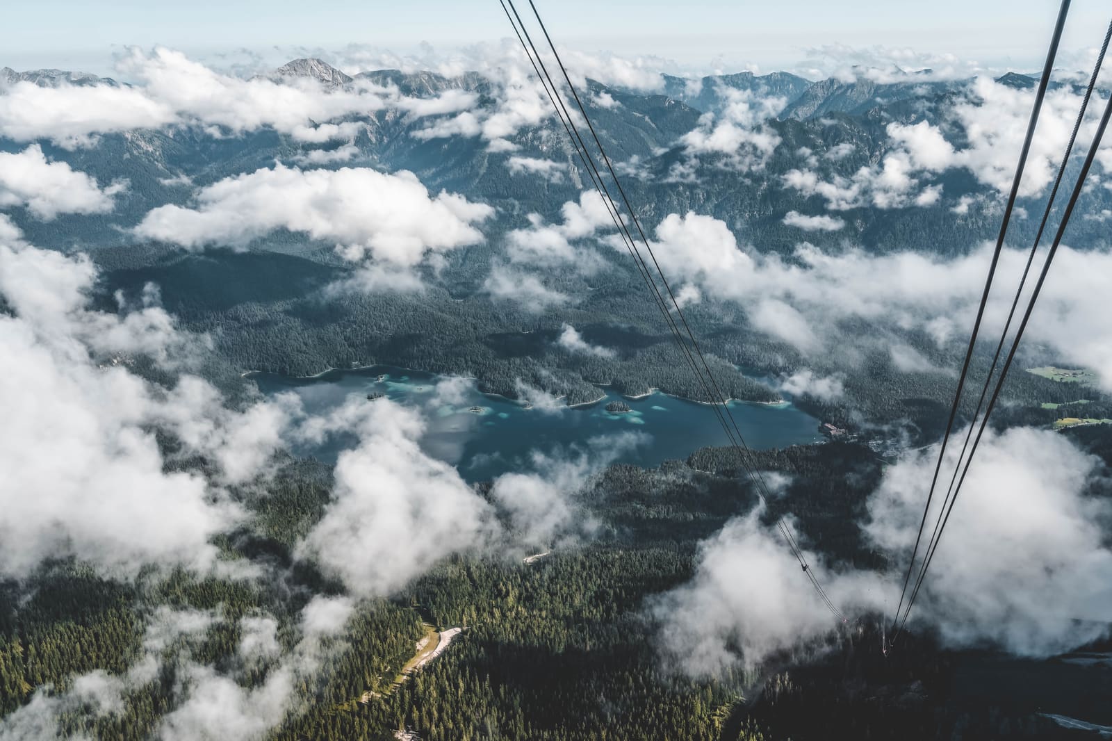 Blick aus der Zugspitz-Seilbahn über Wolken und Wälder auf den Eibsee, eingerahmt von den Tragseilen